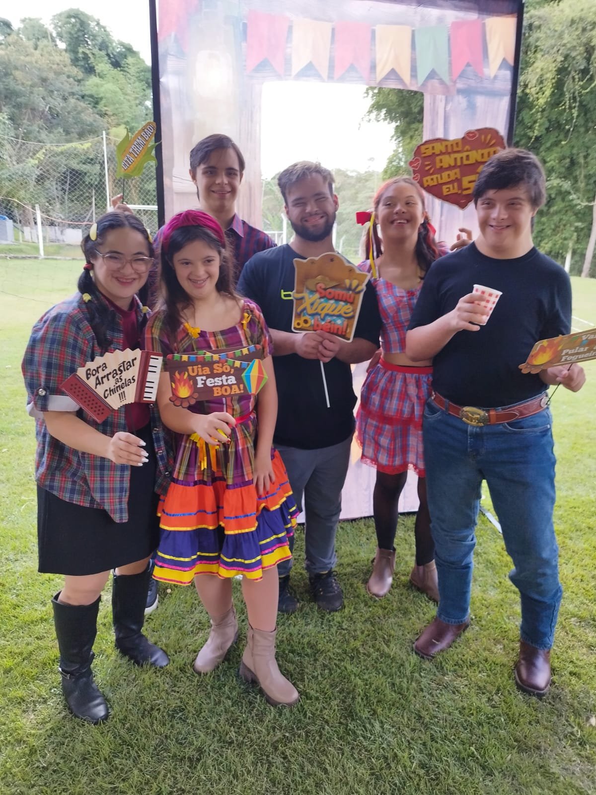Integrantes da APTIC em roupas de festa junina, com plaquinhas divertidas em um gramado.